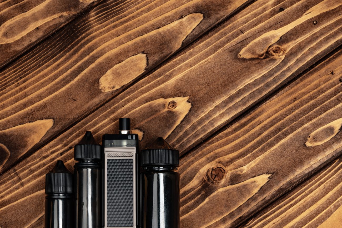 Vape and vape juice bottles on dark brown wooden background