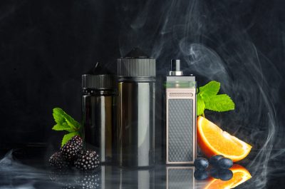 Vape and smoking liquid with fruit against black background with smoke front view